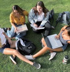 students sitting in circle on grass with laptops on laps